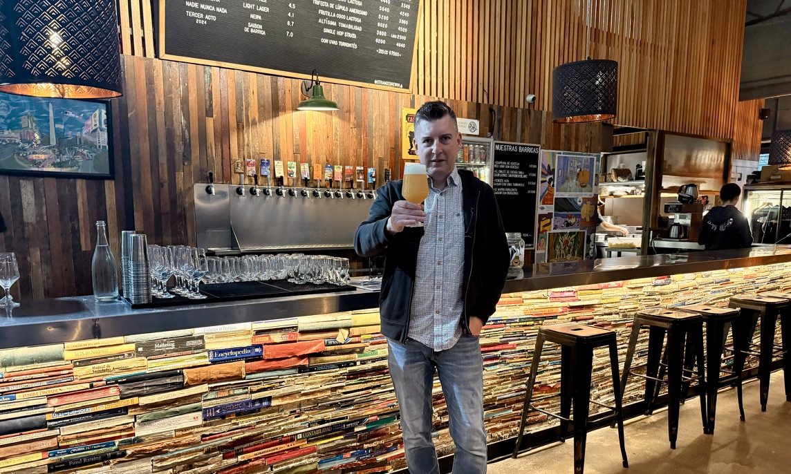 Rob enjoying a beer in Buenos Aires at a taproom with a bar lined with books